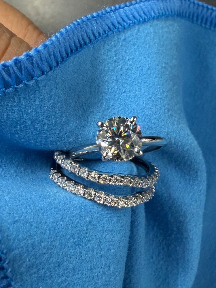 Progress photo of the same round solitaire ring and two diamond bands laid on a blue cloth